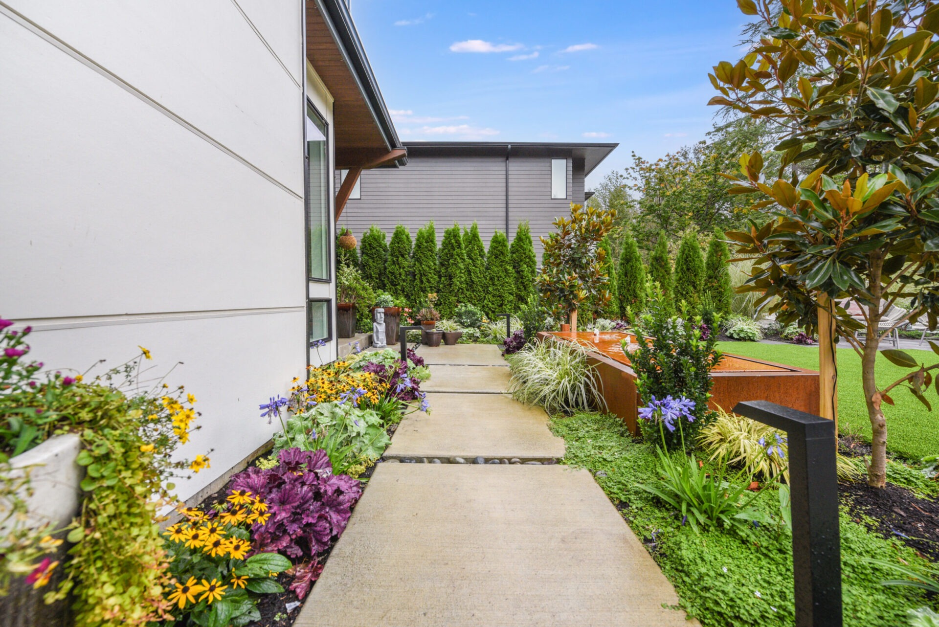 A modern house features a lush garden with colorful flowers and neatly trimmed hedges along its pathway, creating a serene and inviting atmosphere.