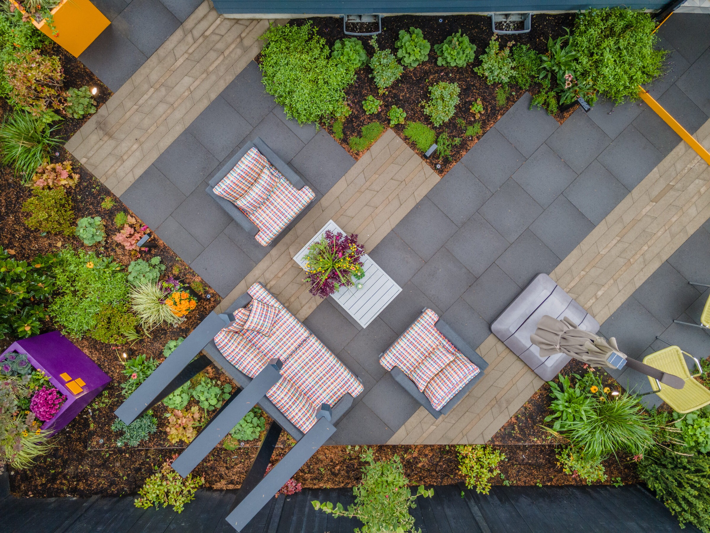 Aerial view of a modern patio with colorful furniture, geometric paving, and surrounding lush greenery. The space is neatly organized and vibrant.