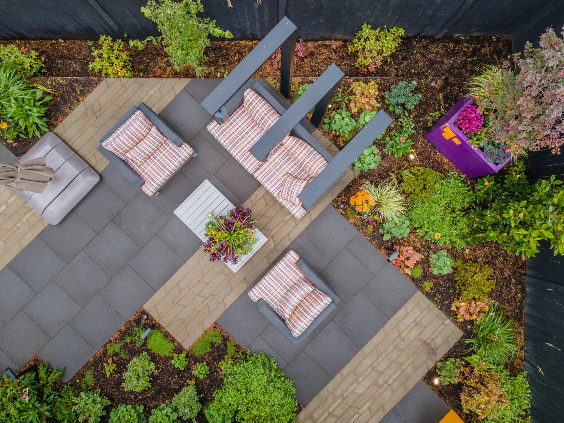 Aerial view of a modern patio with striped cushions, surrounded by vibrant greenery and colorful planters, creating a peaceful garden atmosphere.