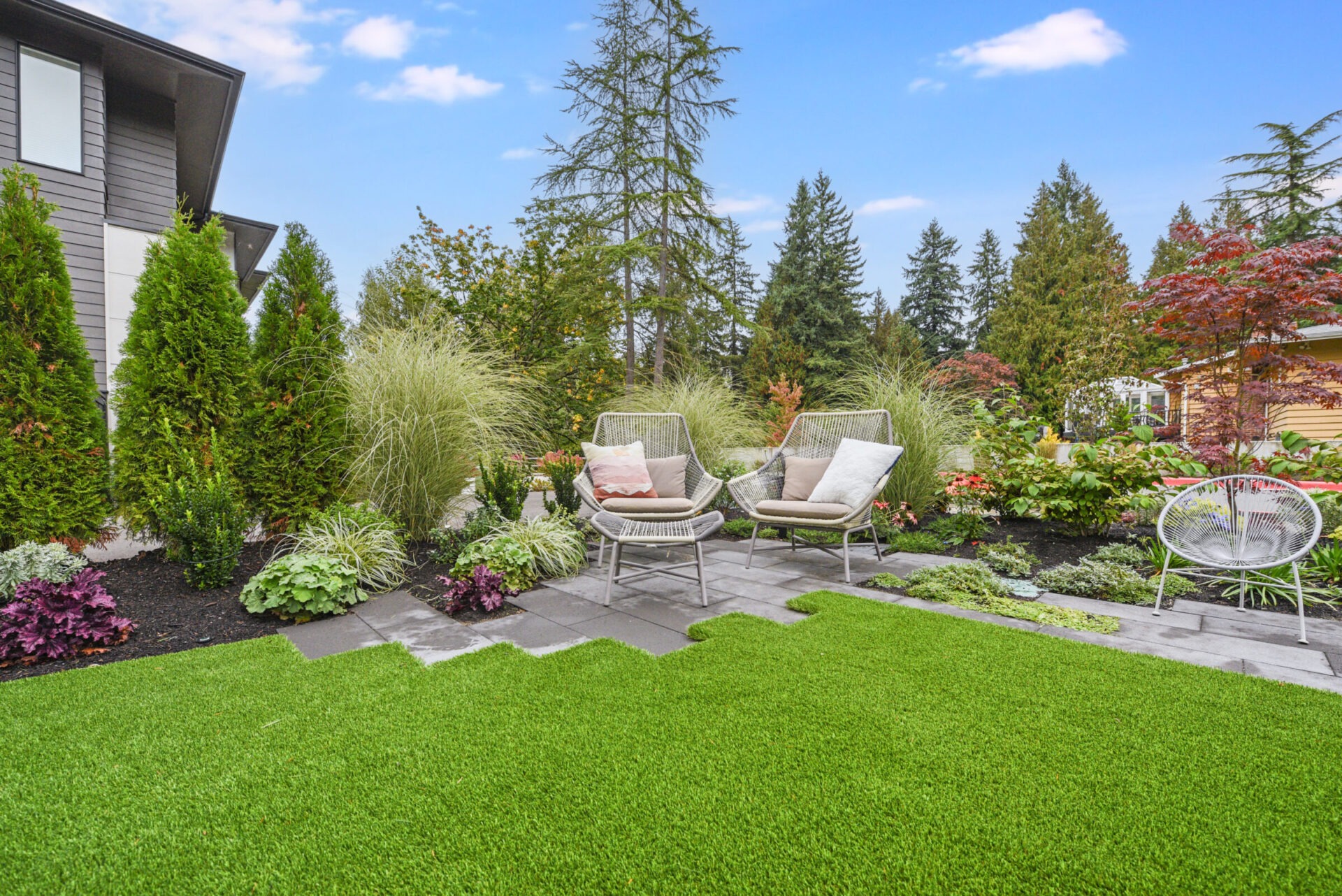 A tranquil garden scene with chairs, lush greenery, and clear blue skies. A perfect space for relaxation and enjoying nature.