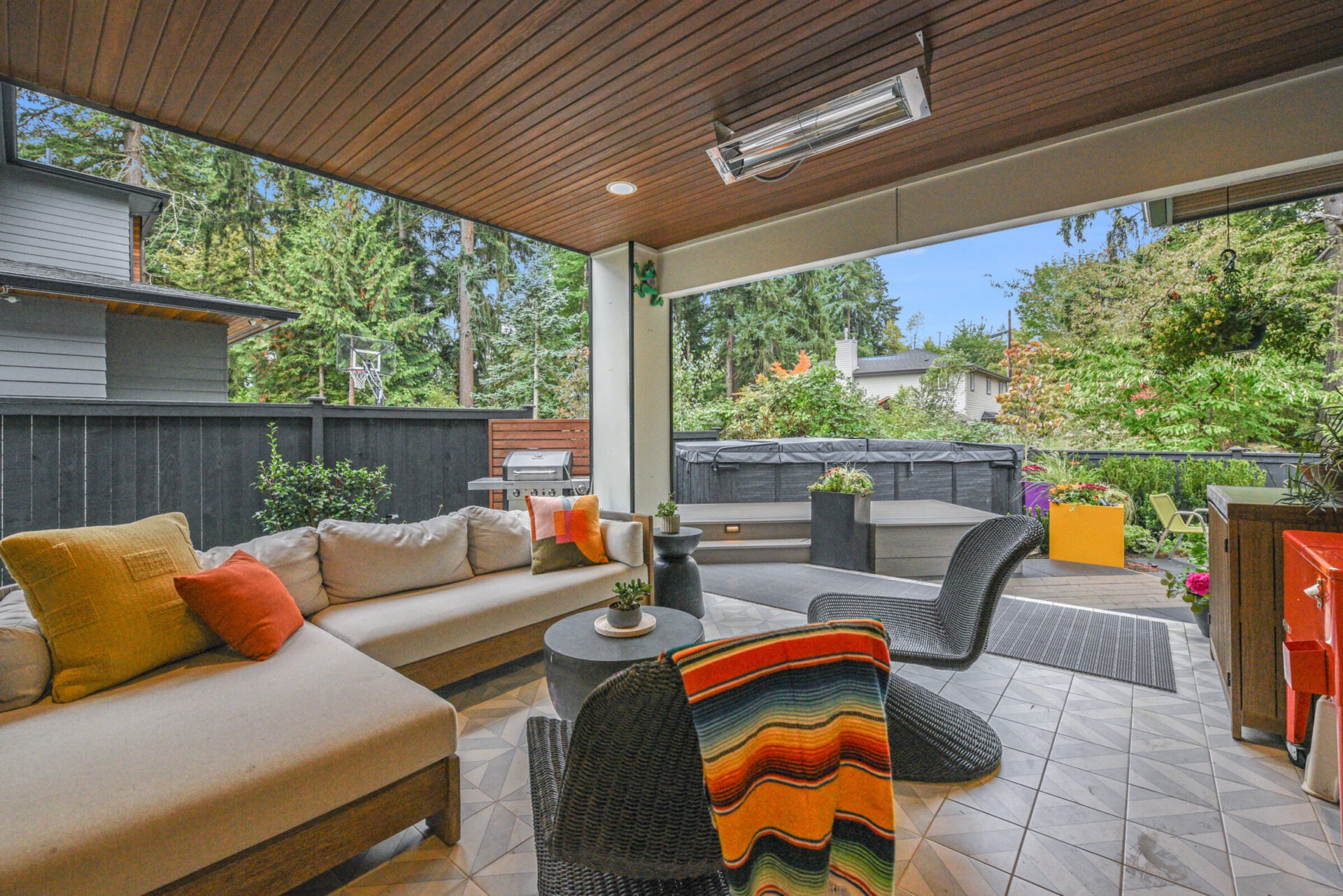 A cozy outdoor patio with seating, colorful cushions, and a vibrant throw blanket. Surrounded by greenery, creating a relaxing atmosphere.