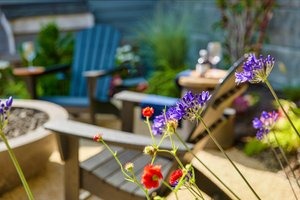 A cozy outdoor seating area features two Adirondack chairs surrounded by vibrant flowers and greenery, creating a peaceful garden retreat.