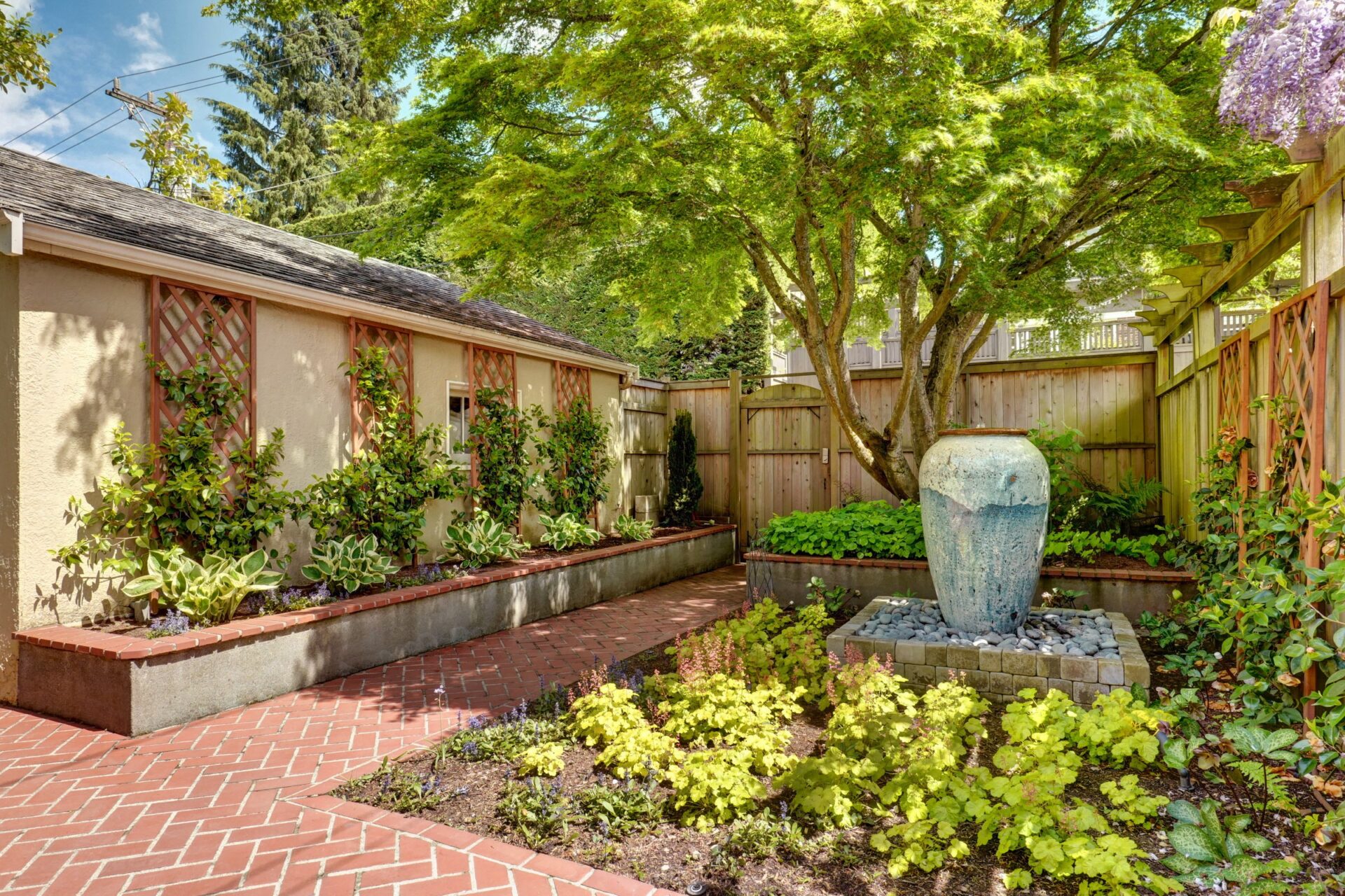 Serene garden scene with a large ceramic vase centerpiece, brick pathway, lush greenery, and wooden fencing surrounding a cozy outdoor nook.