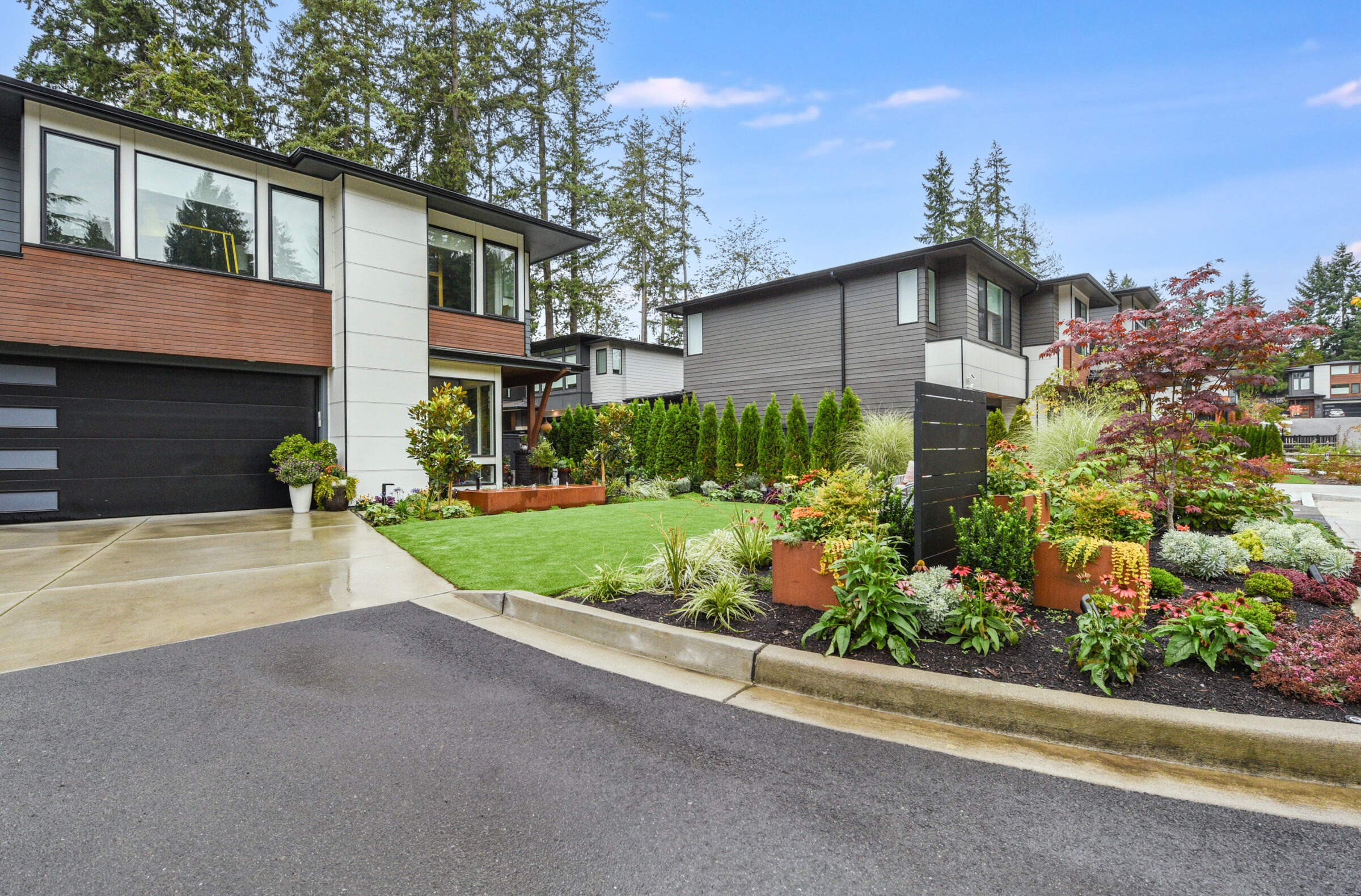 Modern suburban homes with well-maintained gardens and trees in a quiet neighborhood. Overcast sky and no people present.