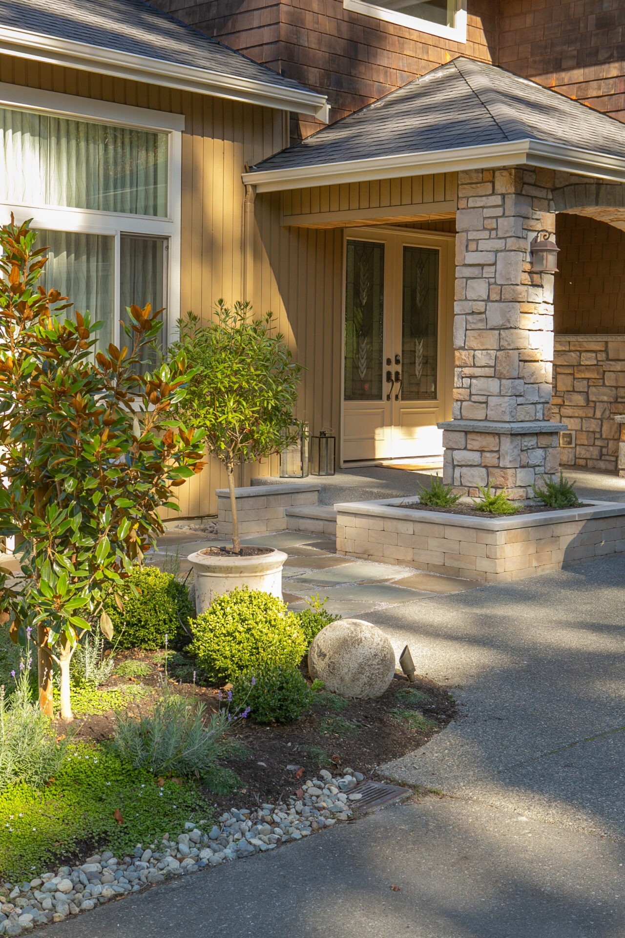 Charming house exterior with stone and wood accents, surrounded by a well-maintained garden featuring various plants and shrubs in bright sunlight.