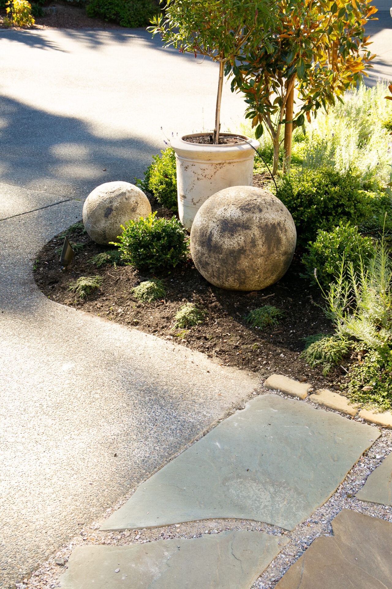 A garden scene features a potted plant, two spherical stones, and surrounding greenery with light illuminating the area. No people are present.