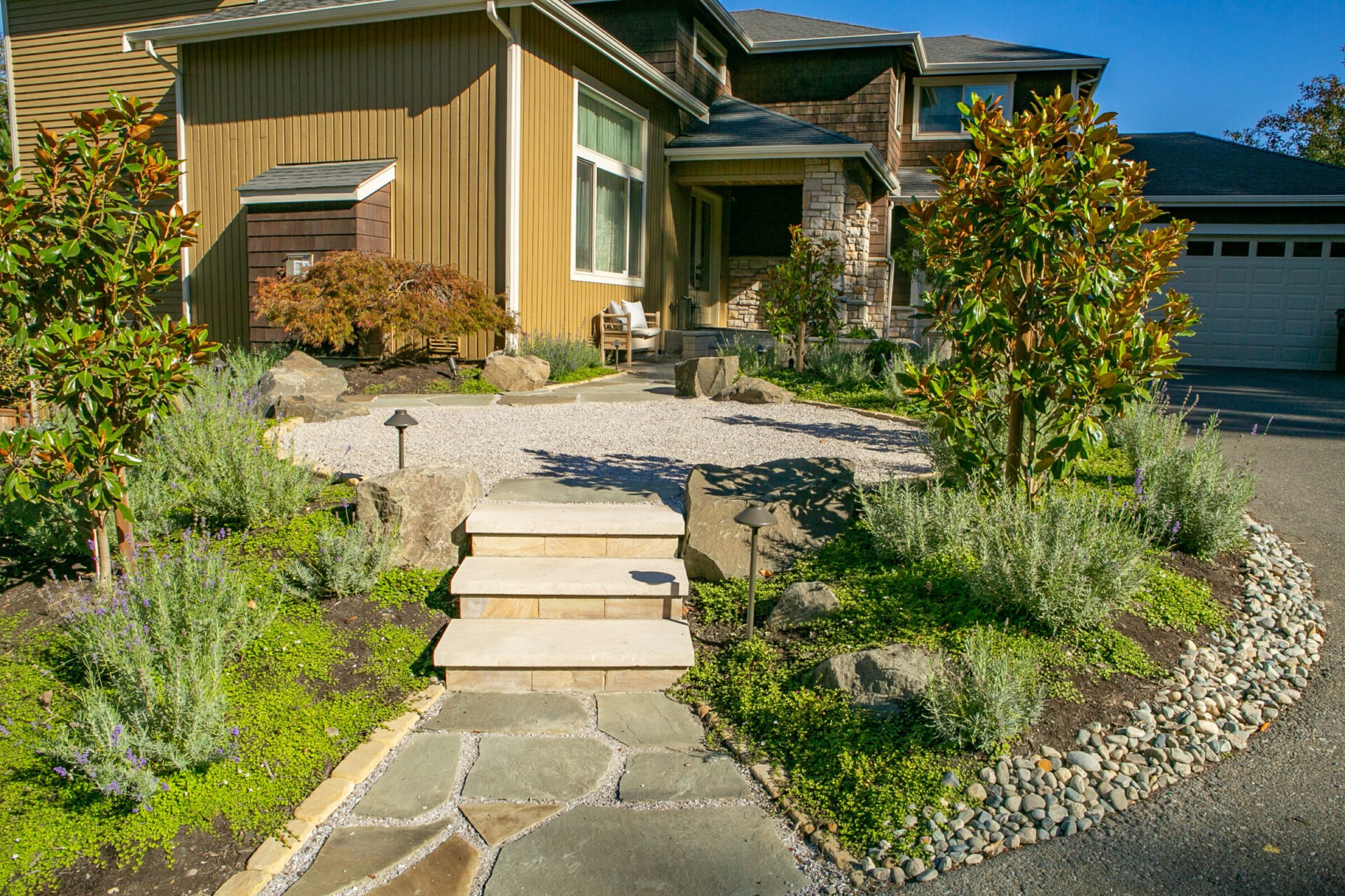 Modern house with stone pathway, landscaped garden, and wooden exterior. Stairway leads to entrance. No people or recognizable landmarks present.