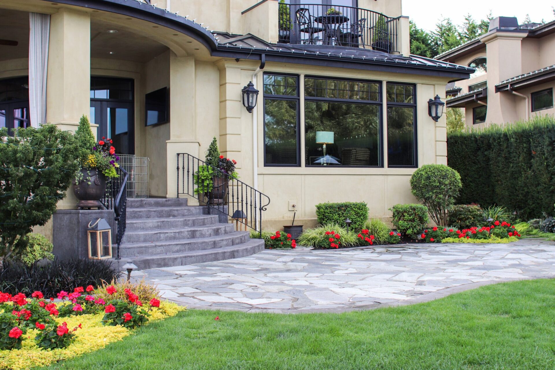 Modern house with a well-maintained garden, stone patio, and large windows. Decorative lanterns and vibrant flowers enhance the inviting entrance.