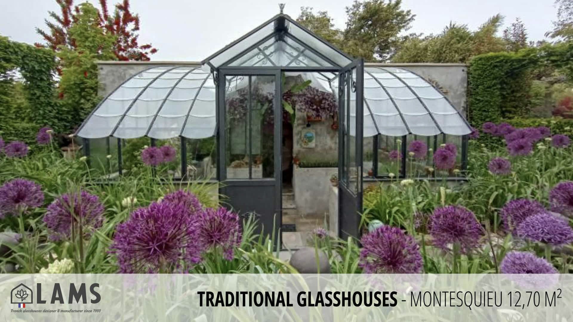 A traditional glasshouse with an elegant design surrounded by lush greenery and vibrant purple flowers in a picturesque garden setting.