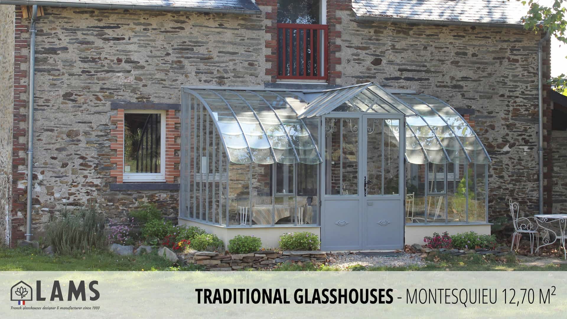 Stone house features a traditional glasshouse extension with arched windows. Ornamented garden and metal seating create a charming, rustic ambiance.