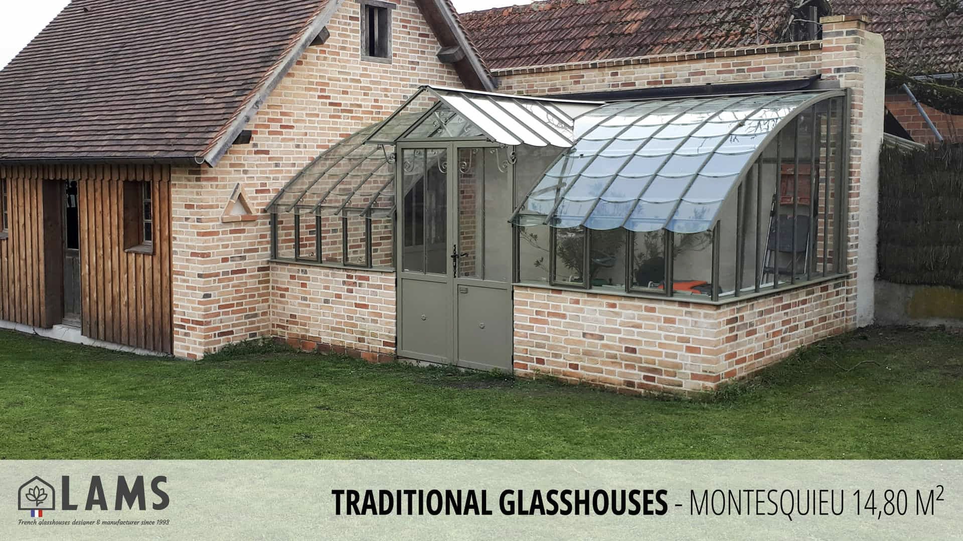A brick and glass traditional greenhouse attached to a rustic house, surrounded by grass. LAMS branding is visible at the bottom.