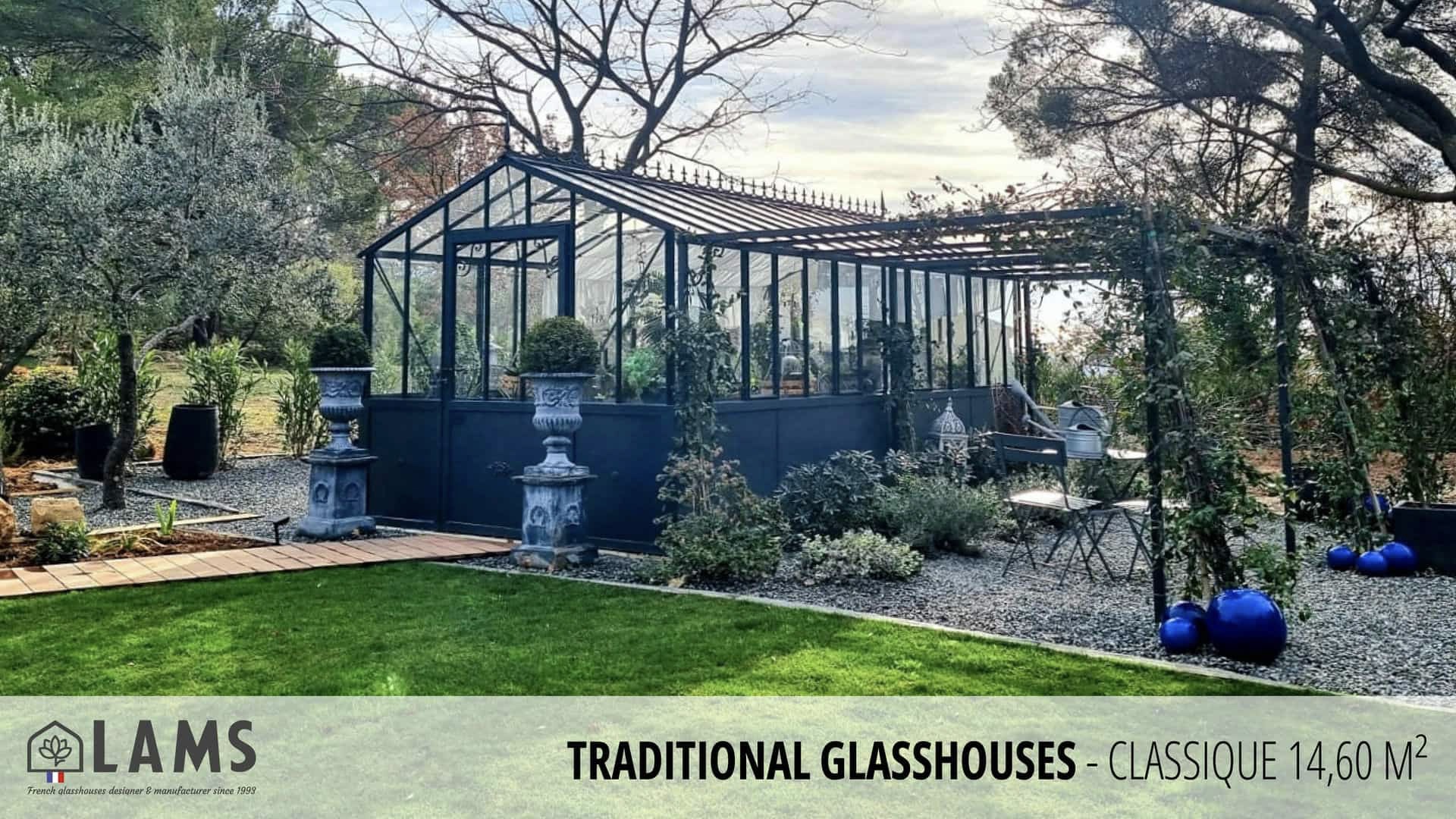 A traditional glasshouse in a garden setting, surrounded by trees and shrubs, with decorative urns and blue spherical ornaments displayed outside.