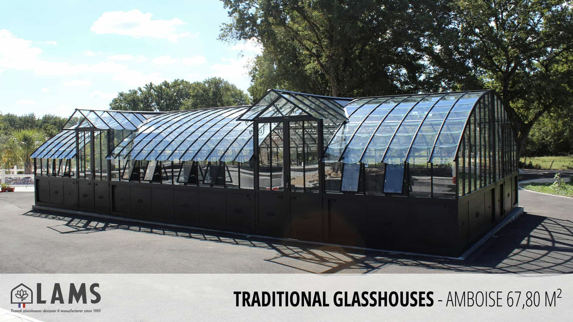 A modern, spacious glasshouse with a metal frame sits outdoors under a clear sky, surrounded by trees. Designed by LAMS, covers 67.80 m².