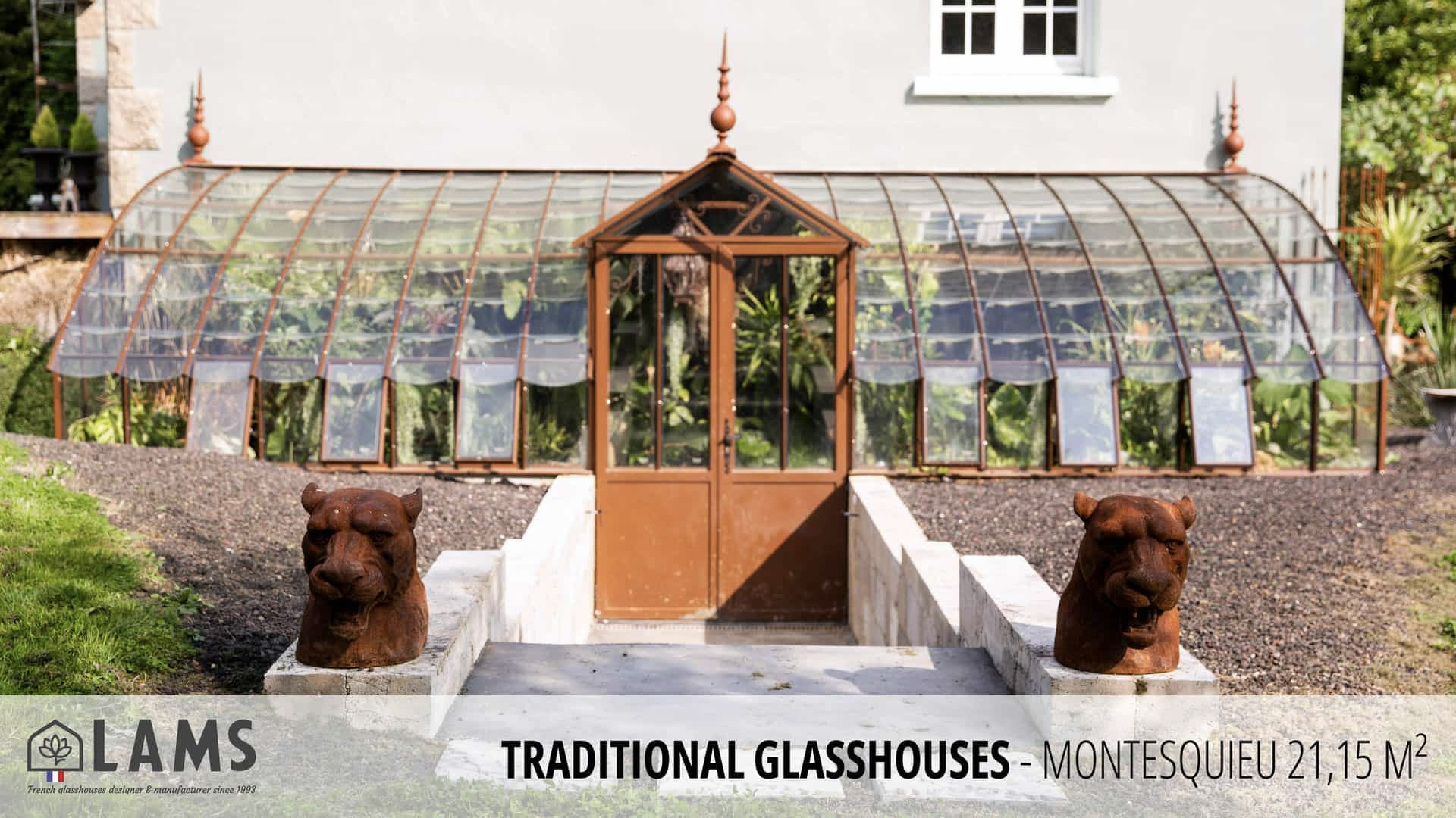 A traditional glasshouse with a curved roof stands between two decorative sculptures, featuring clear panels and an elegant entrance.