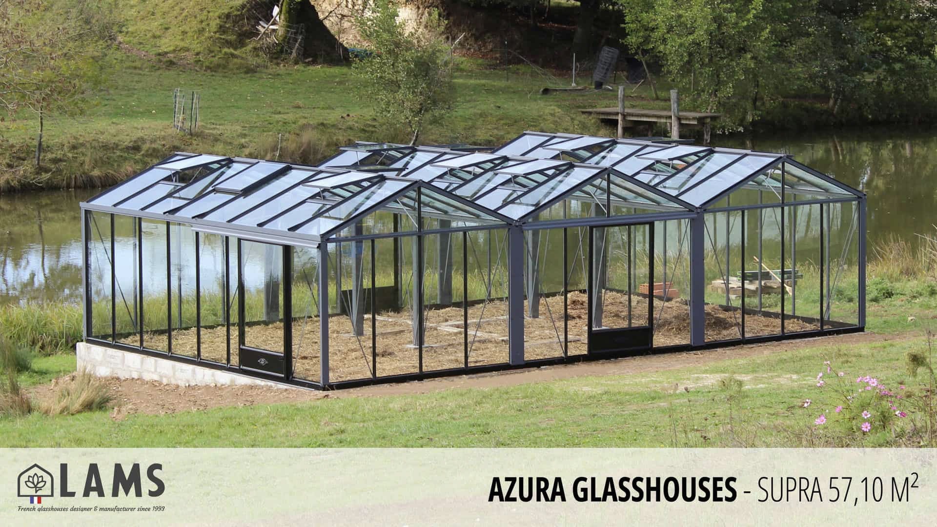 A modern glasshouse sits by a pond amidst lush greenery, reflecting the tranquil natural surroundings. LAMS branding appears in the corner.