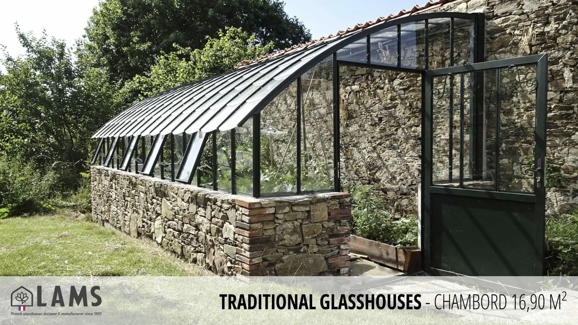 A traditional glasshouse with a stone base and metal frame stands in a lush garden. LAMS logo is displayed in the corner.