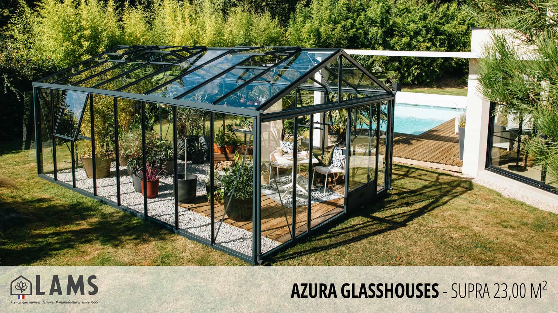 A modern glasshouse with plants inside is next to a pool, surrounded by greenery. There are chairs and a table visible.